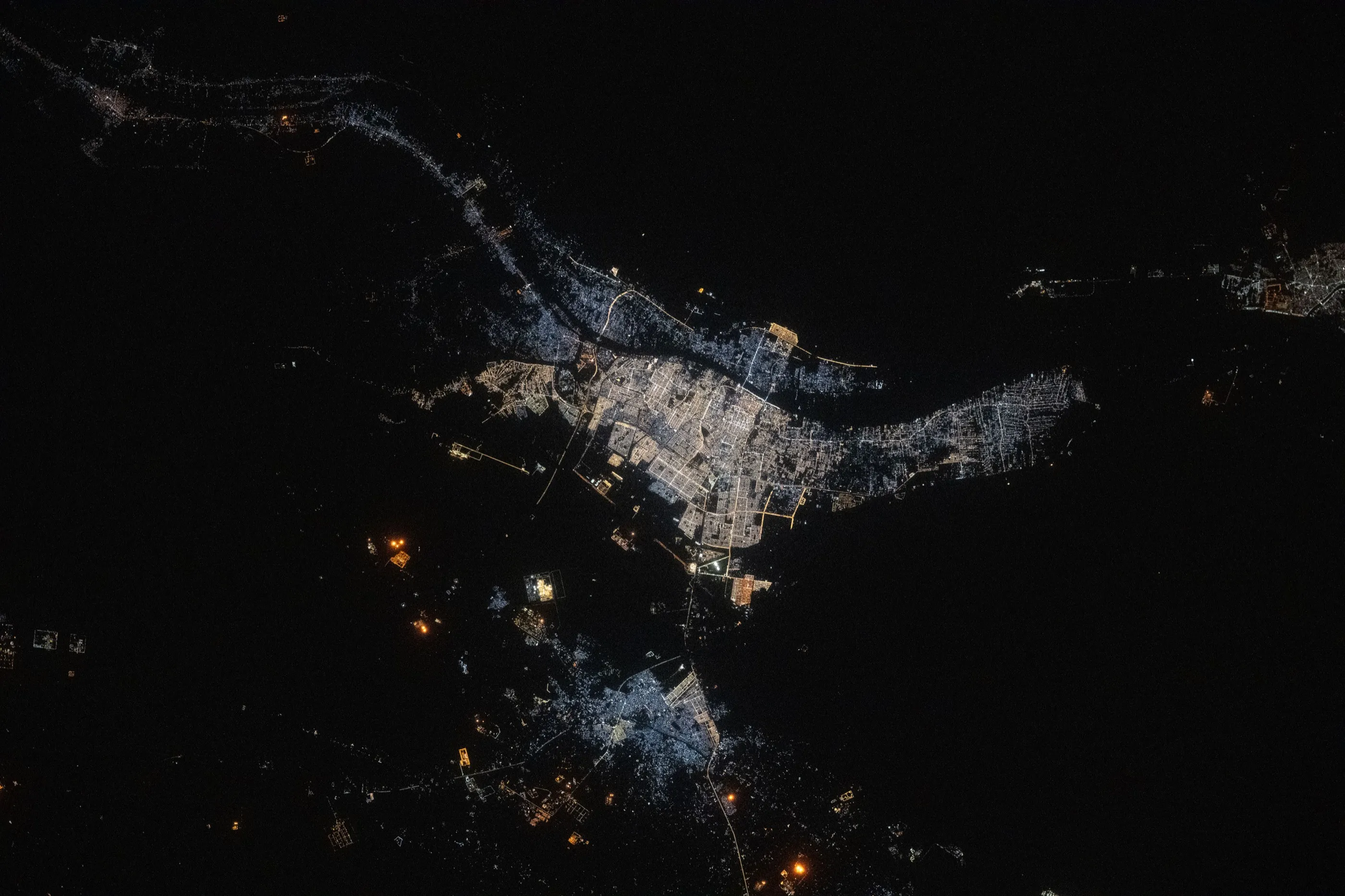The lights of a city on a river, seen from orbit at night.