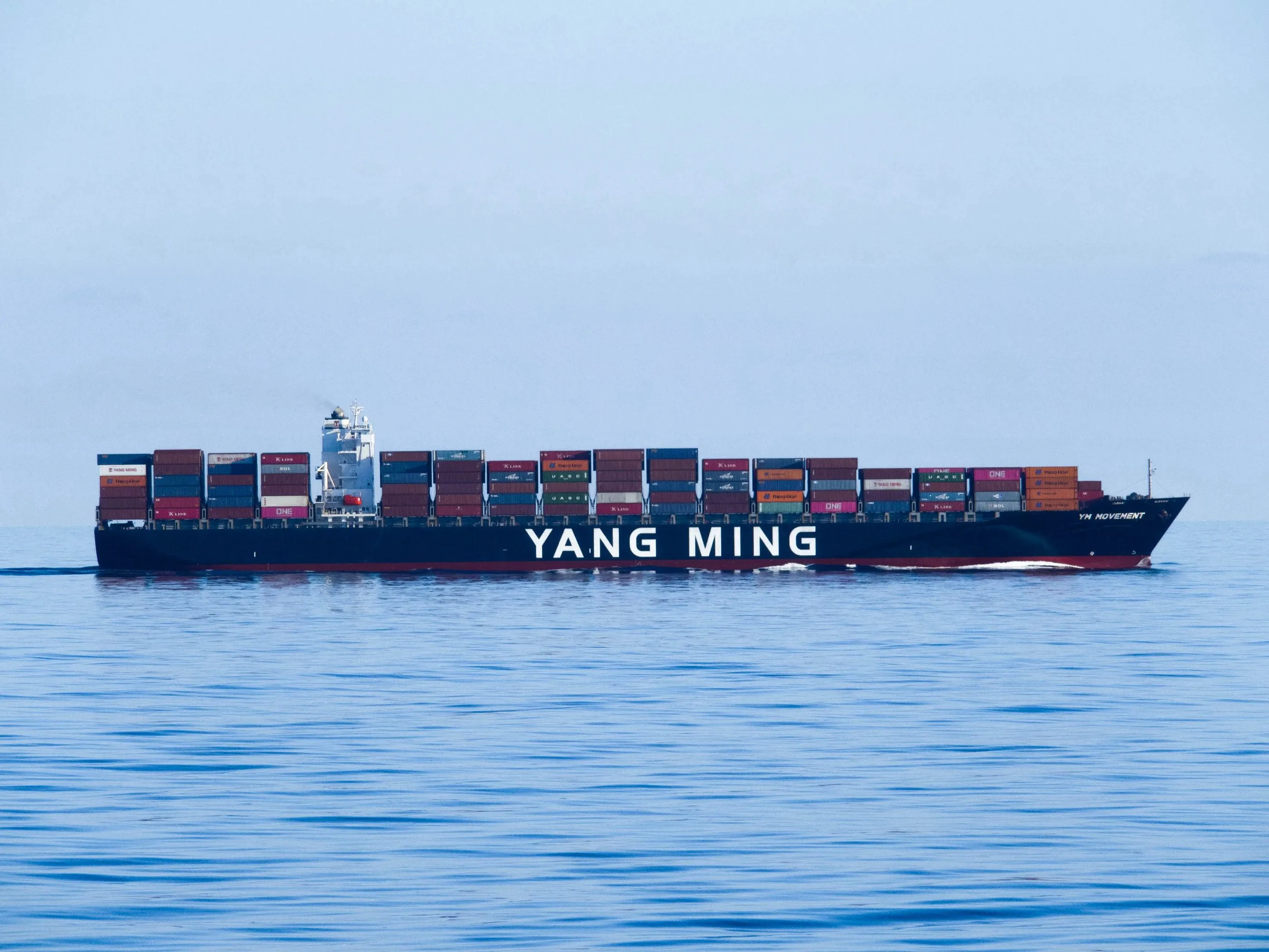 A container ship under way on a flat blue sea.