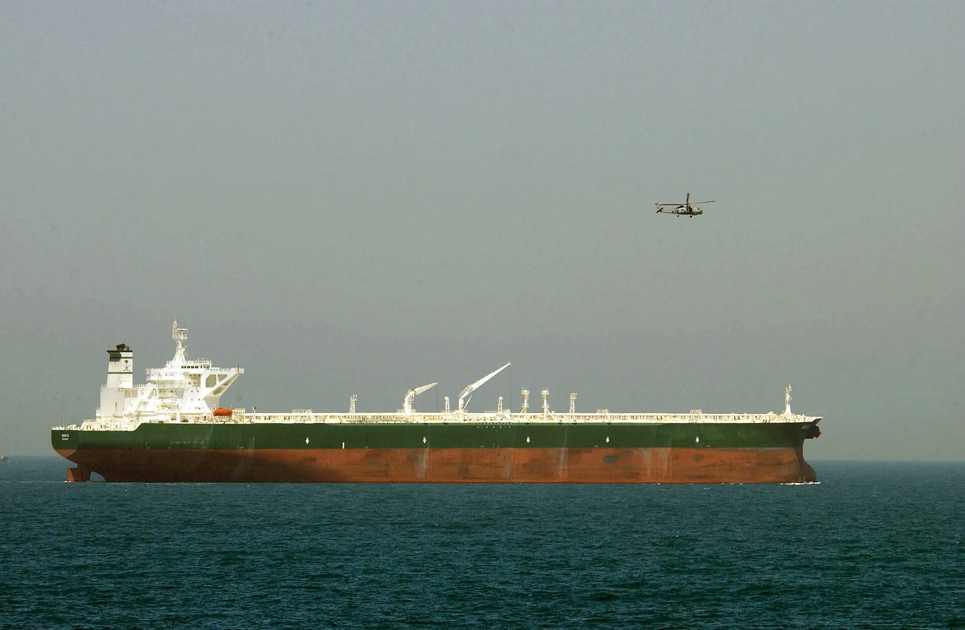 A navy helicopter flies escort over a loaded supertanker in the Gulf.