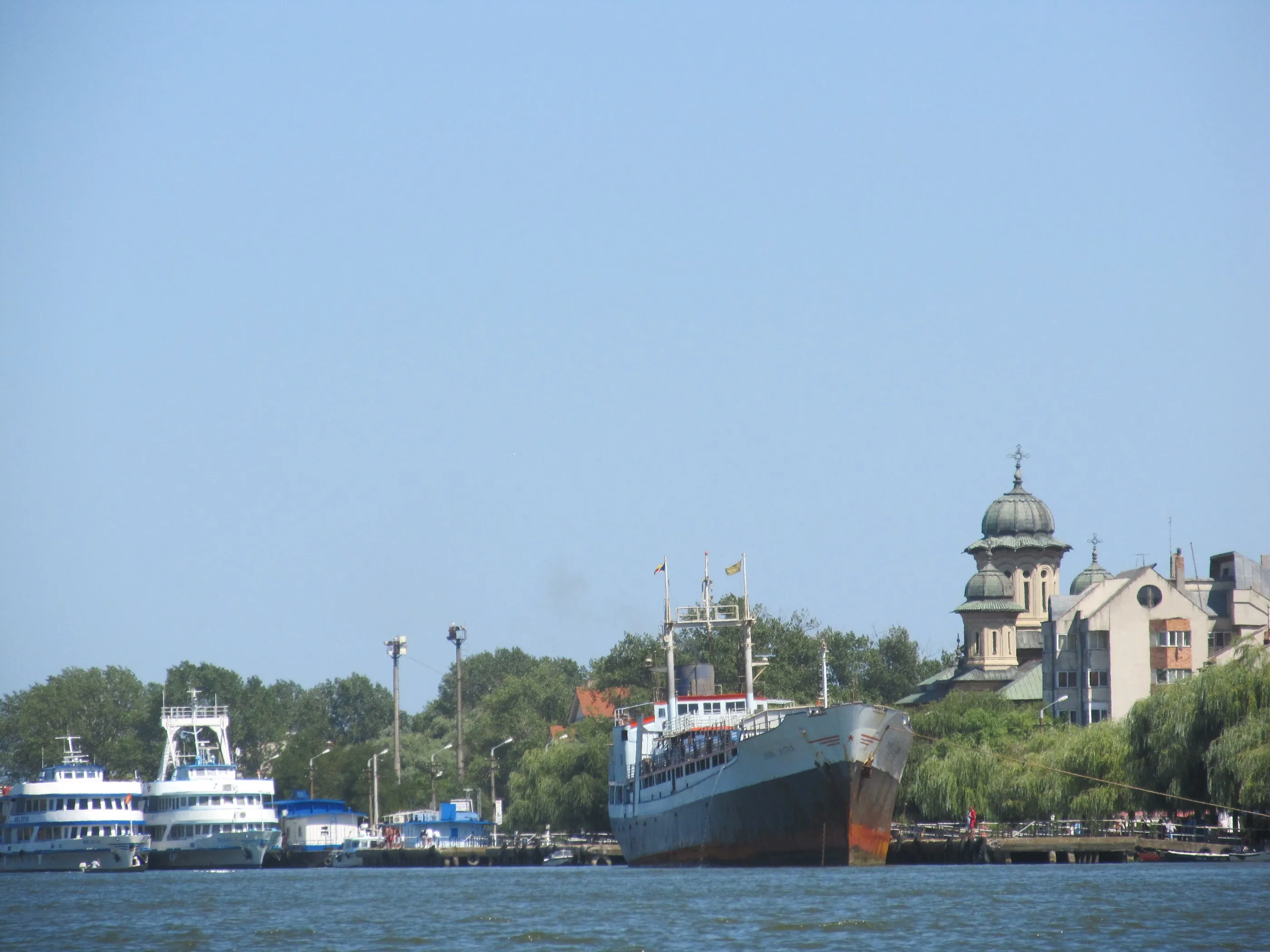 A cargo ship moored on a river beside a small town with a domed church.